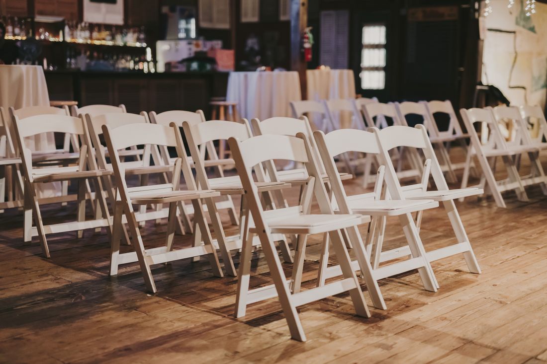 Rows of empty white folding chairs arranged on a wooden floor in a quiet indoor venue before an event