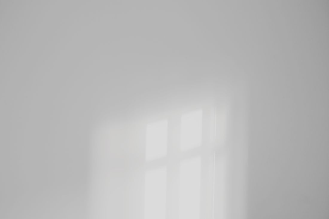 Soft window-shaped daylight and shadow falling across a plain gray interior wall, with no people or objects in frame.