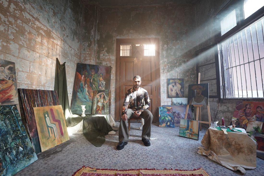 An artist seated in a bright studio surrounded by colorful paintings