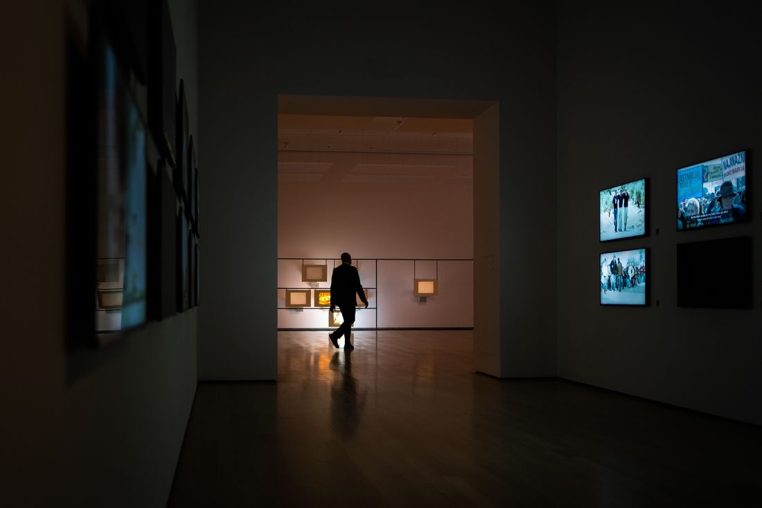 A silhouetted visitor walking through a dimly lit gallery past illuminated artworks