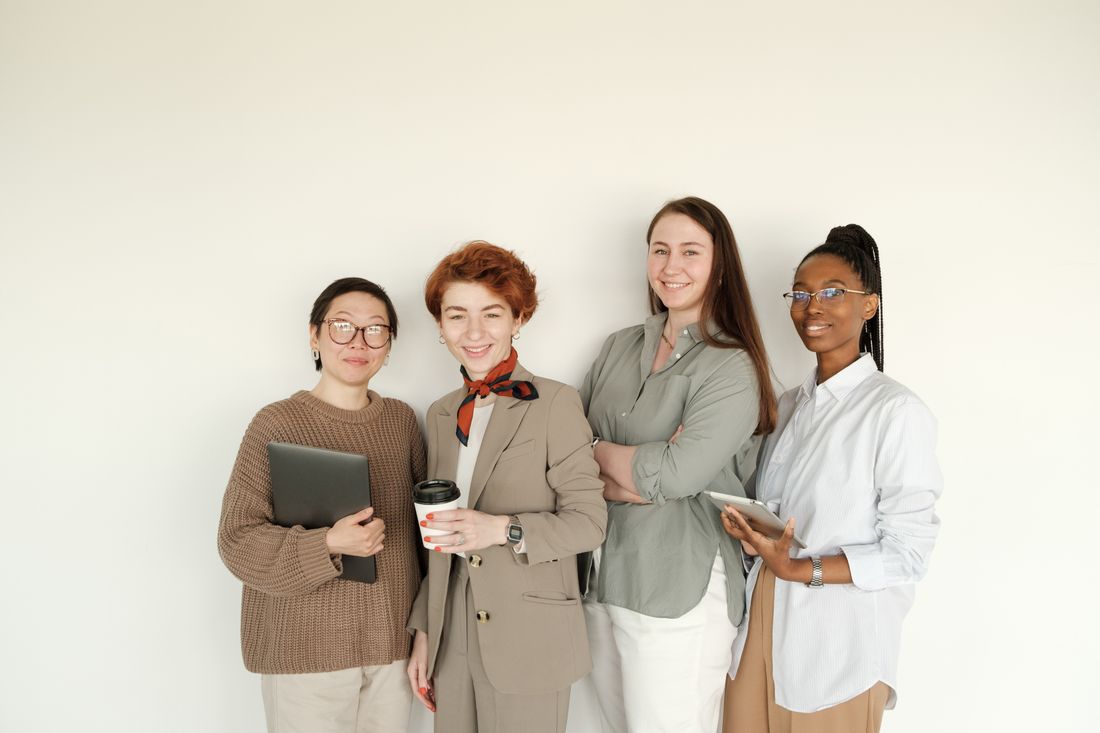 Four colleagues in casual professional clothing standing together against a plain wall, smiling toward the camera