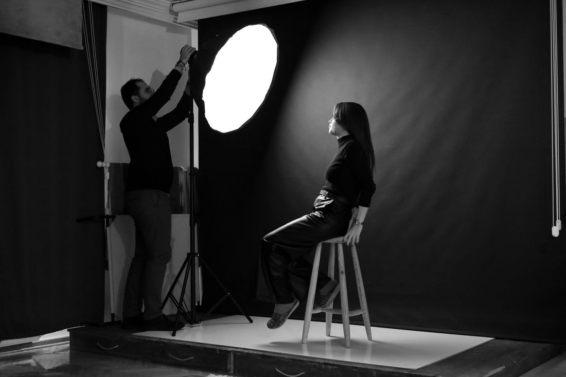 A photographer adjusting a studio light above a seated subject during a portrait session