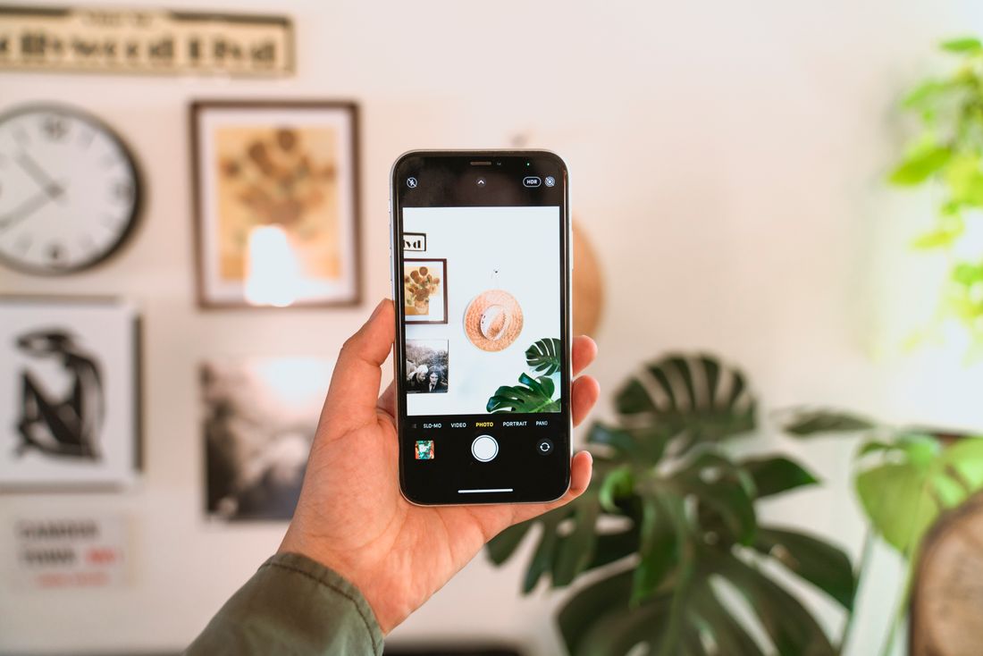 A hand holding a phone photographing a wall of small framed pieces in a casual daytime room