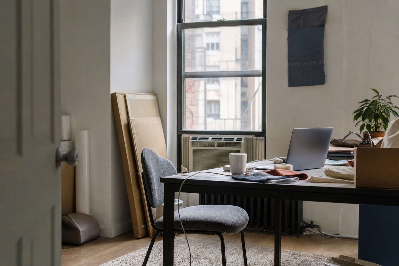 Contemporary creative workspace with a portrait chair, material samples, an angled laptop, cables, and useful location context