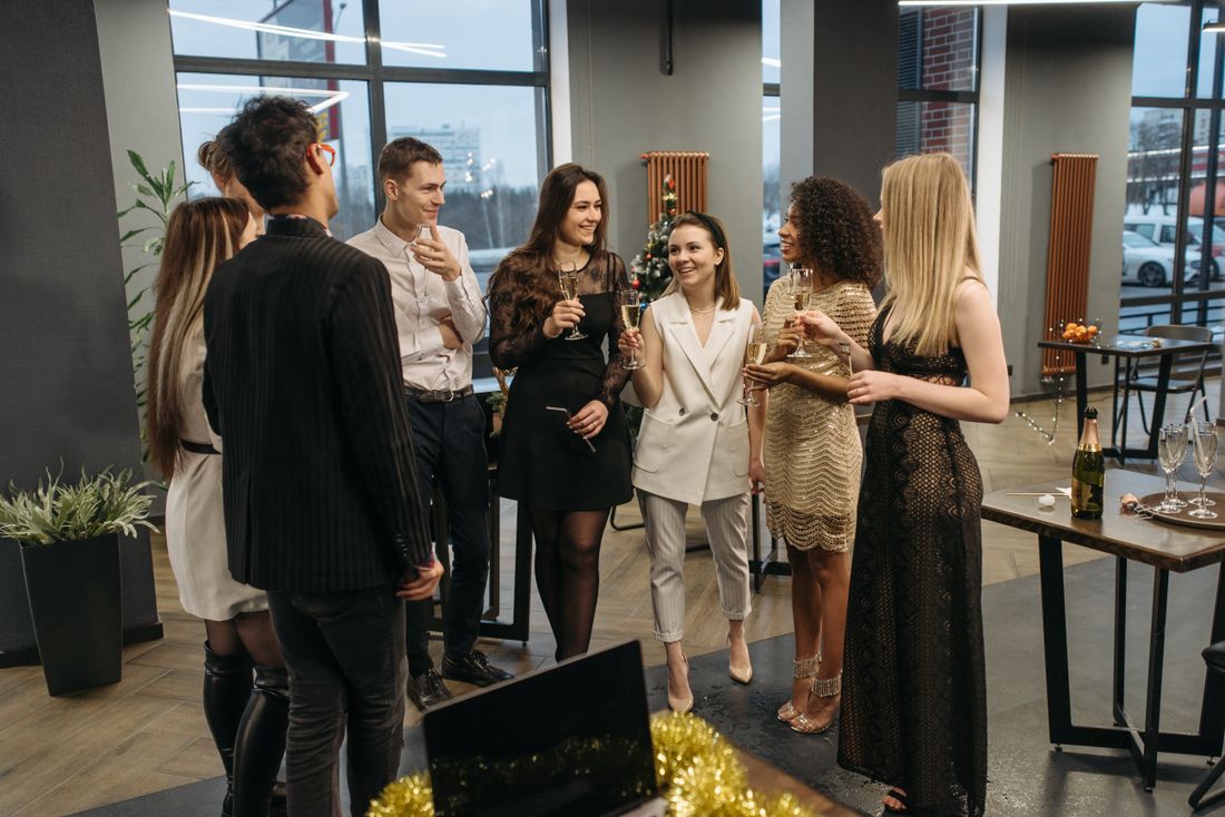 A group of coworkers in cocktail attire mingling with champagne glasses in a decorated office space during a holiday party