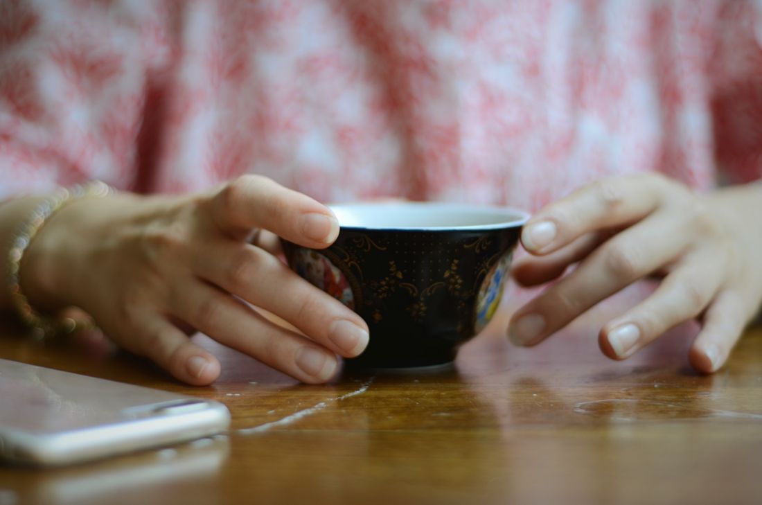 Two hands cupping a small handmade ceramic bowl resting on a wooden table.