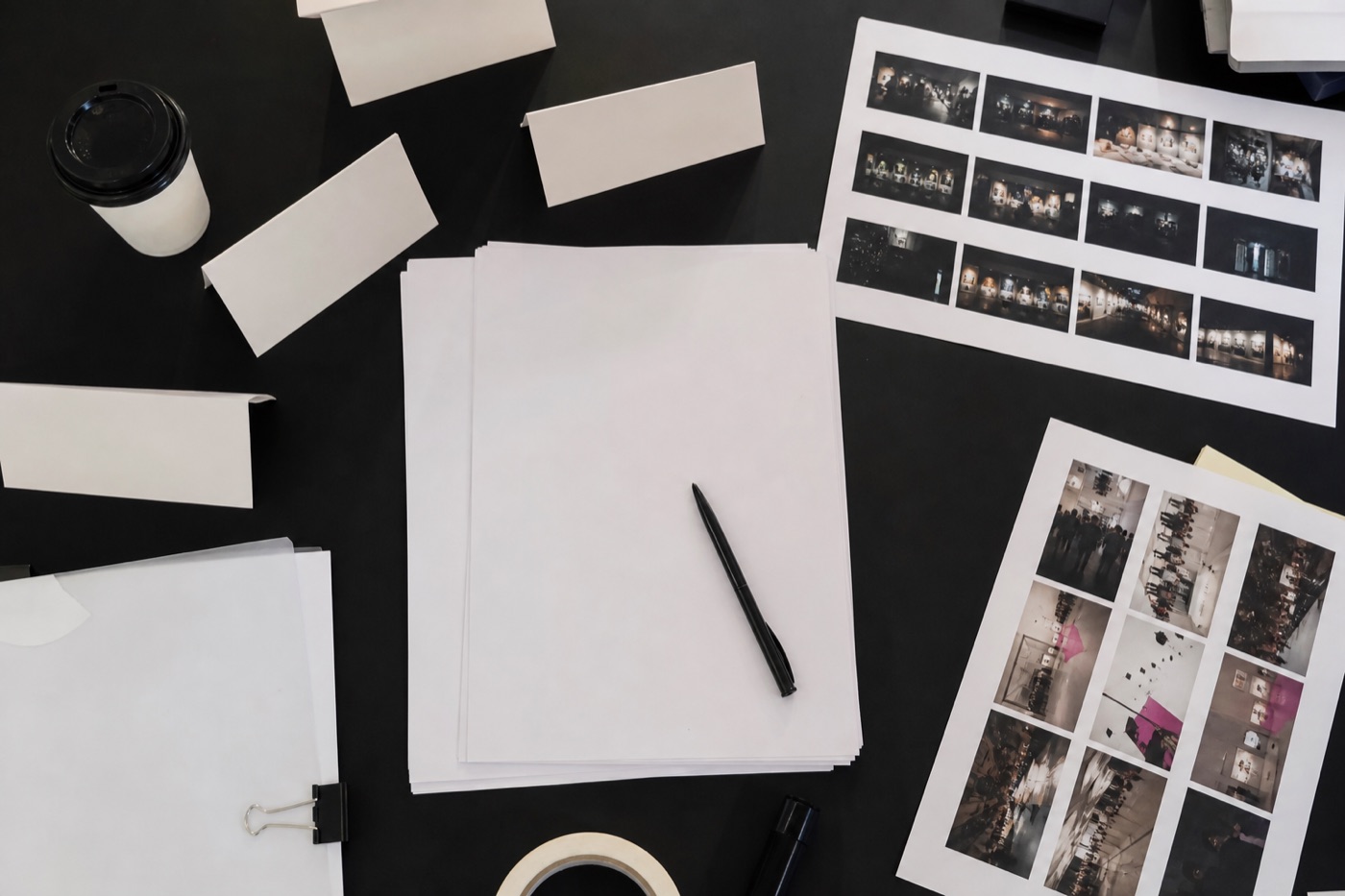 Overhead event delivery planning table with blank run-of-show pages, name cards, coffee, tape, and printed contact sheets