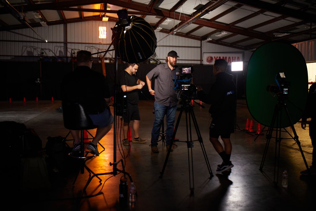 A film crew setting up lighting and camera equipment on a production set in a warehouse studio