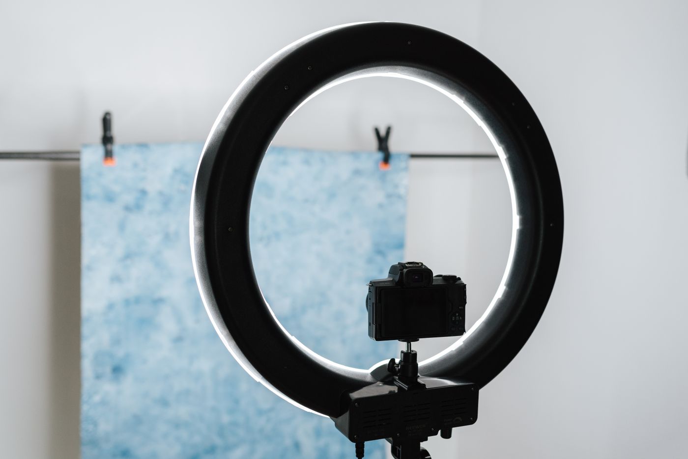 Camera and ring light set up in front of a plain backdrop in a small studio