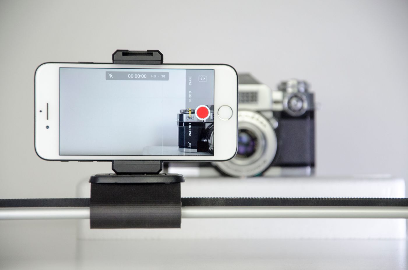 Smartphone mounted on a slider rig recording, with a vintage camera positioned in the background