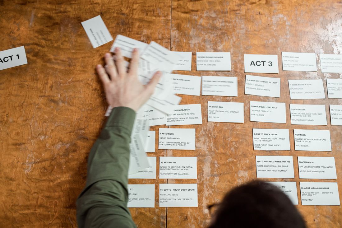 Hands arranging labeled story cards on a wooden table to map out a film's structure in acts.