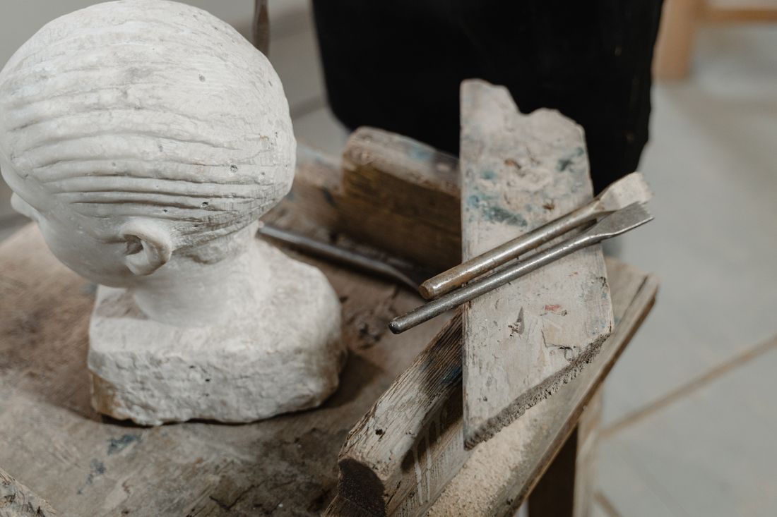 A plaster sculpture head resting on a wooden worktable beside sculpting tools in an artist's studio