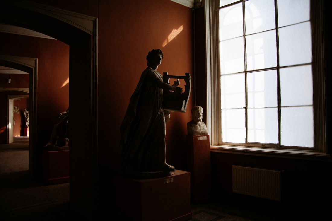 A classical sculpture in silhouette as afternoon sunlight pours through a large museum window