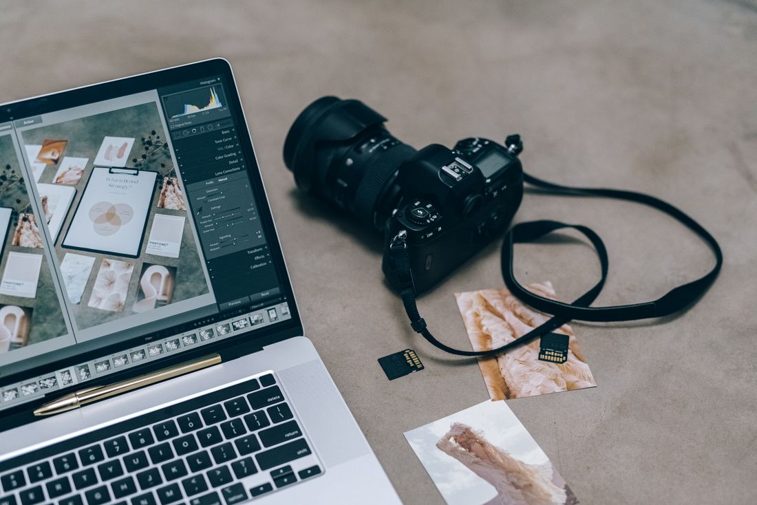 Laptop with photo editing software open next to a DSLR camera and memory cards on a desk
