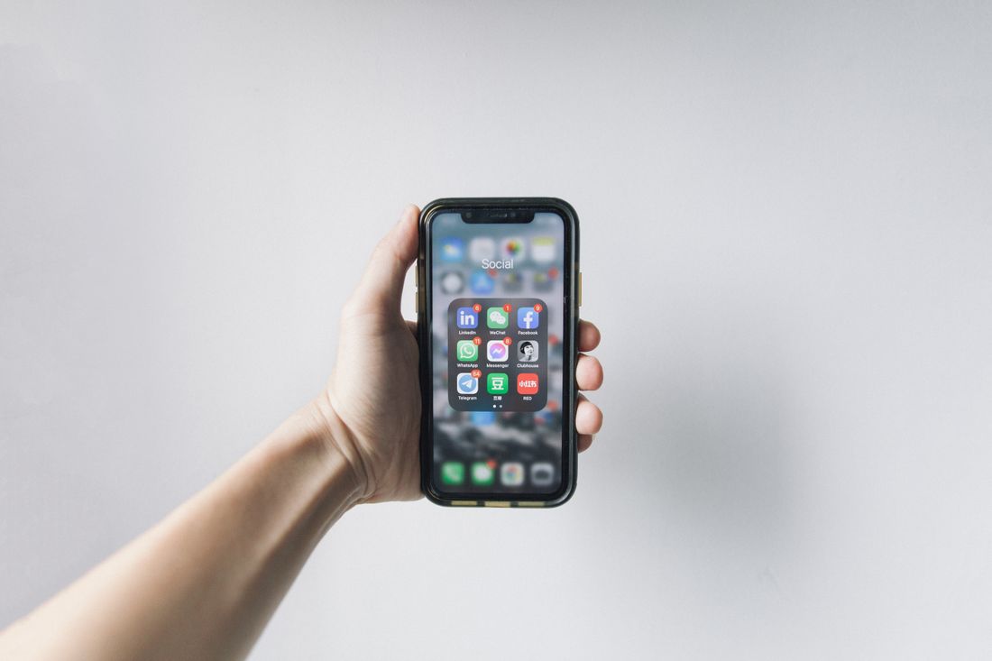 A hand holding a smartphone showing a home screen with social media apps