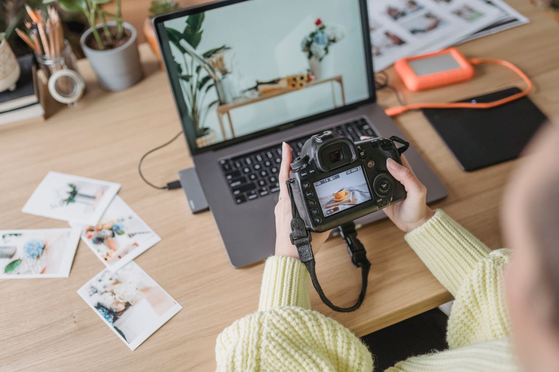 Overhead view of a photographer reviewing an image on a camera screen next to a laptop and printed photos on a desk