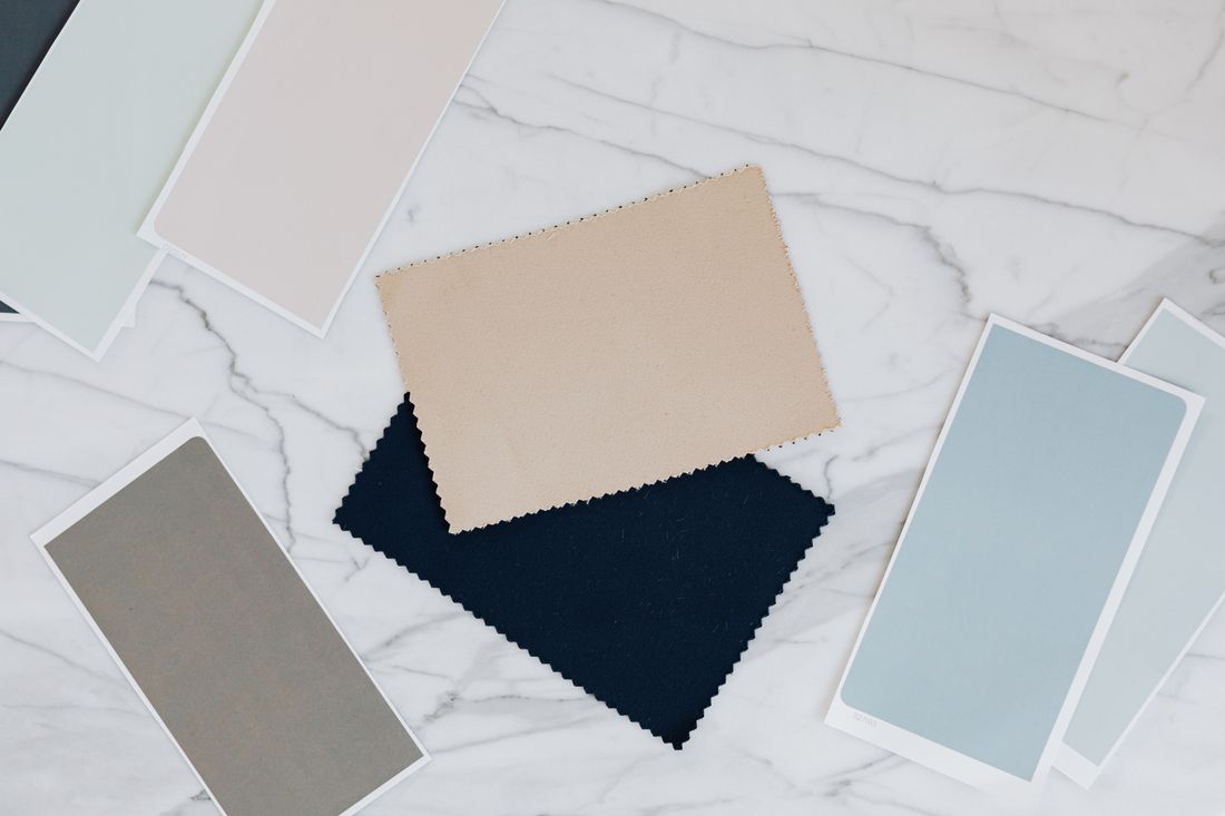 Folded fabric swatches and paint color palette cards laid out together on a marble table