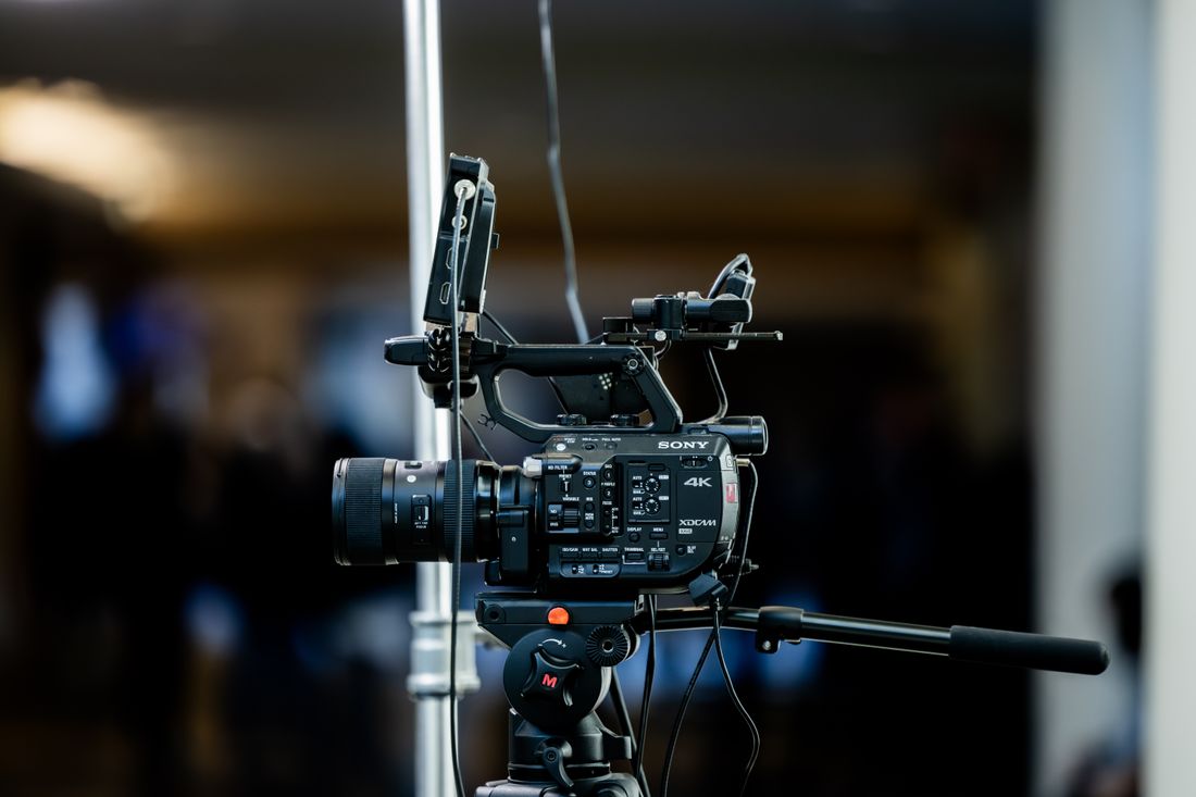 A video camera on a tripod set up at the back of a dimly lit room before an event