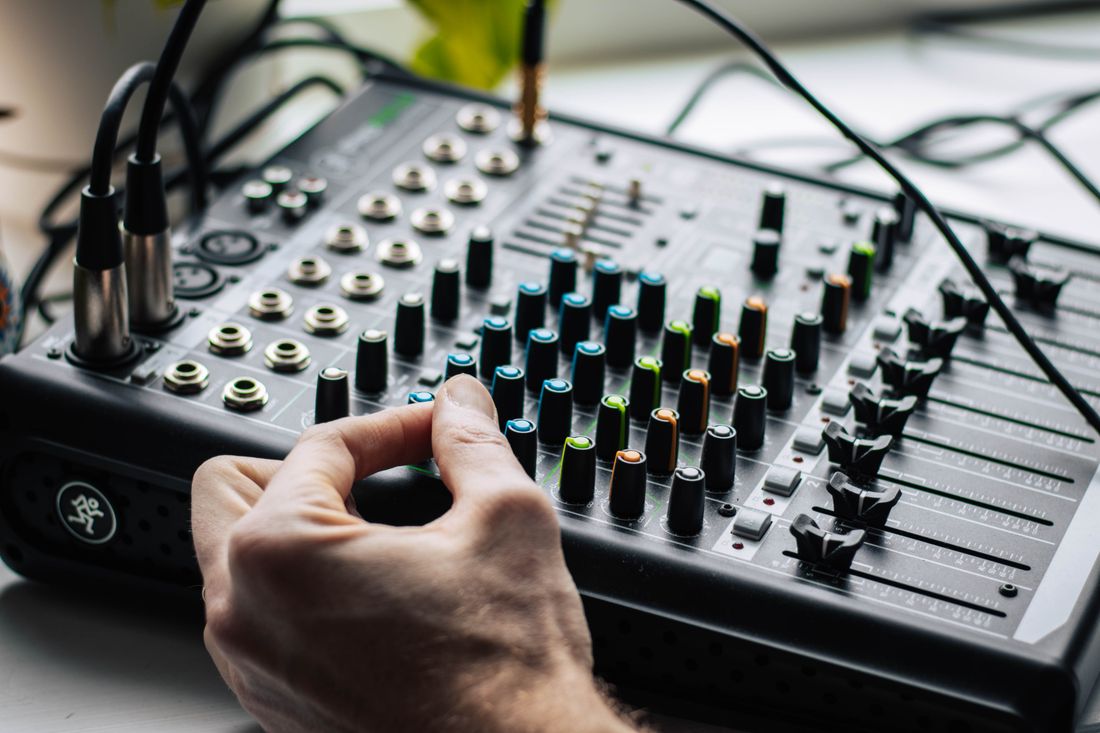 A hand resting on the faders of a small audio mixing desk