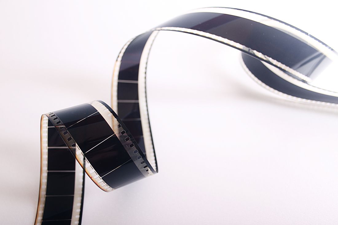 A curled, unexposed strip of camera film with visible sprocket holes, shot against a plain white background.