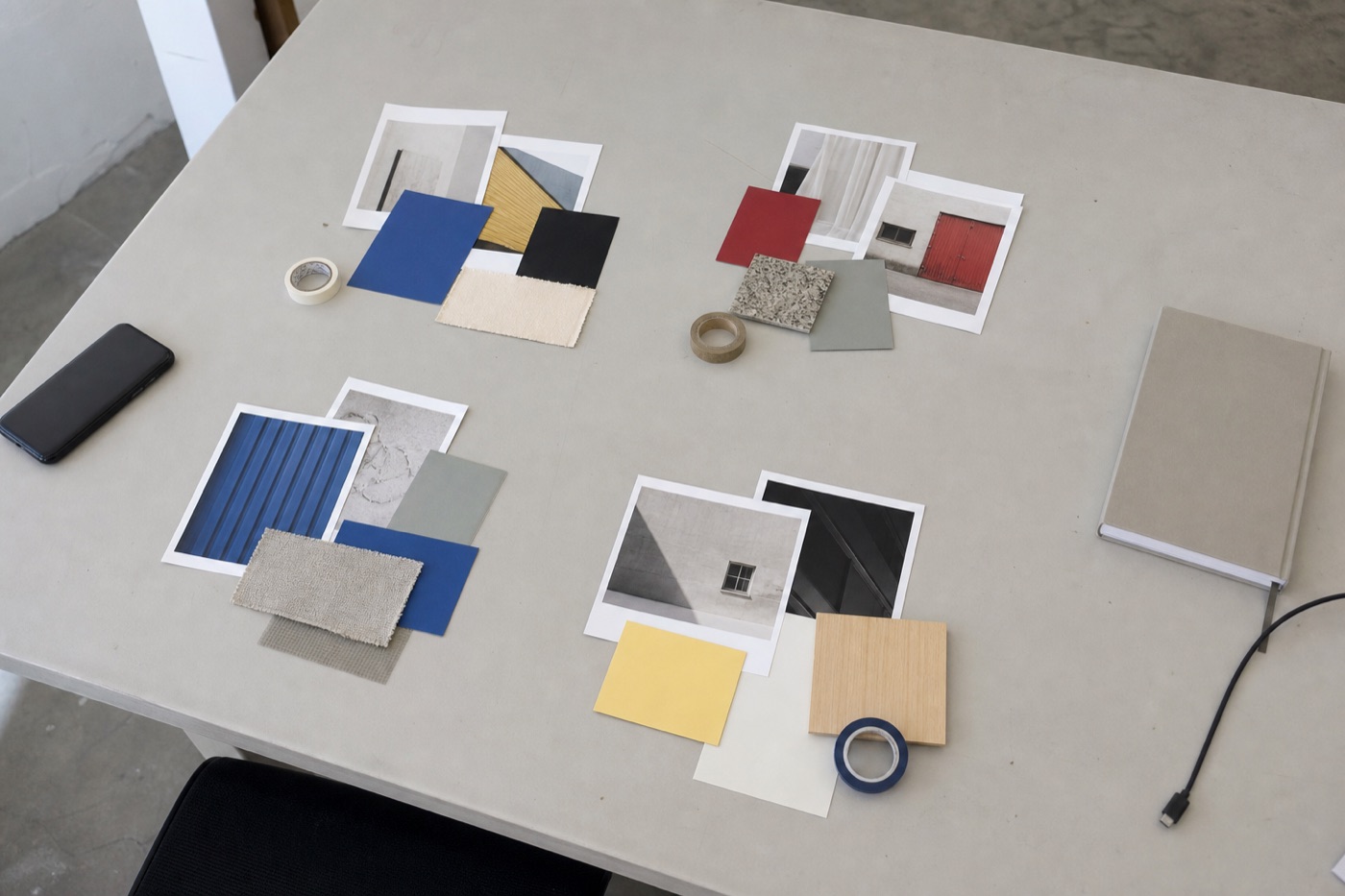 Overhead view of four recurring content groups made from image prints, color cards, material samples, tape, a notebook, phone, and cable