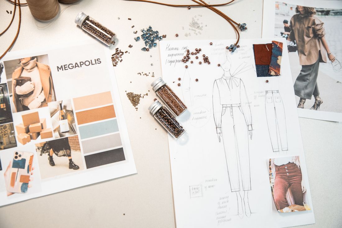 A fashion workspace with a color palette, garment sketch, fabric photos, and reference tear sheets laid out together on a desk.