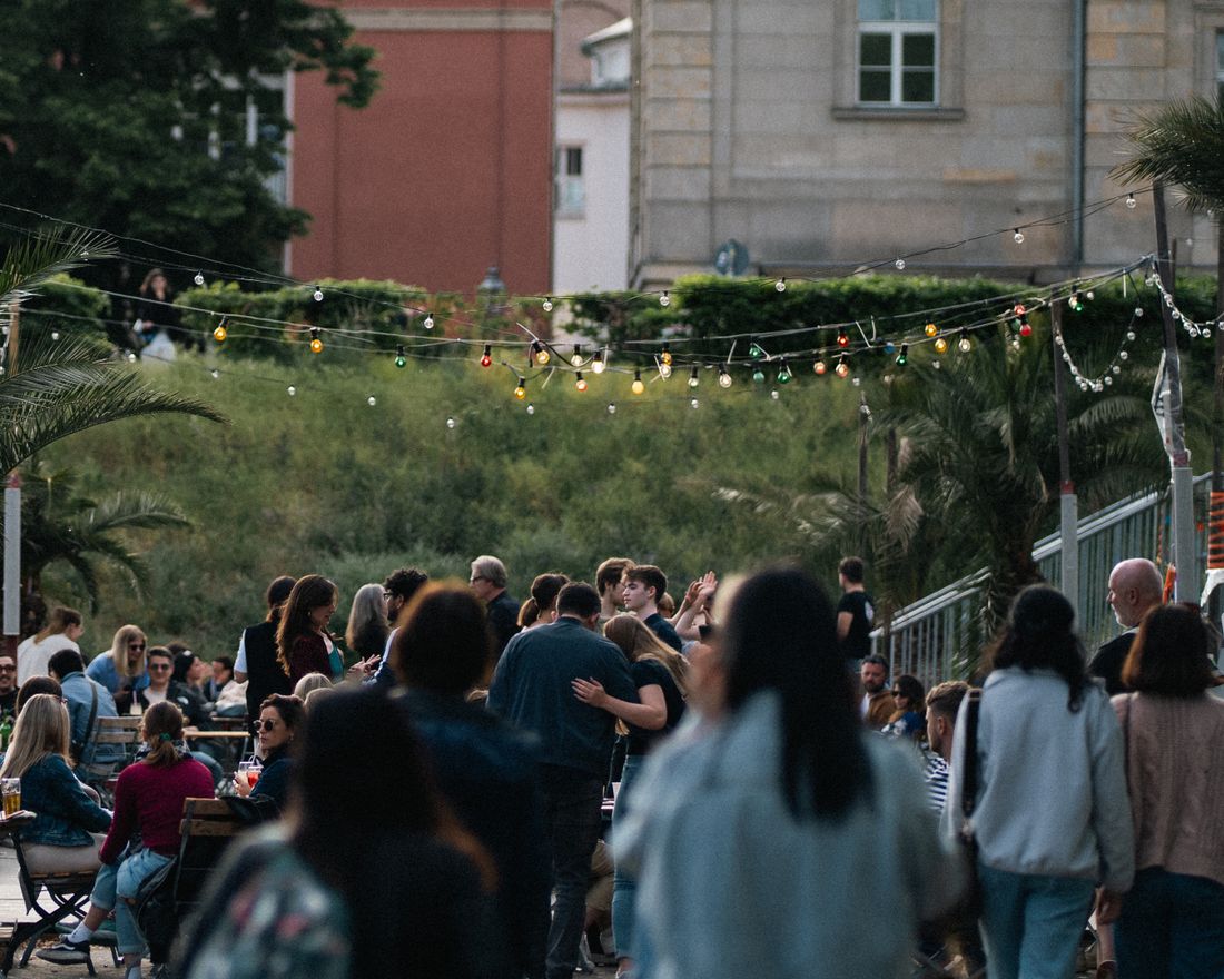 A crowd gathered outdoors in the evening under strings of lights at a community gathering