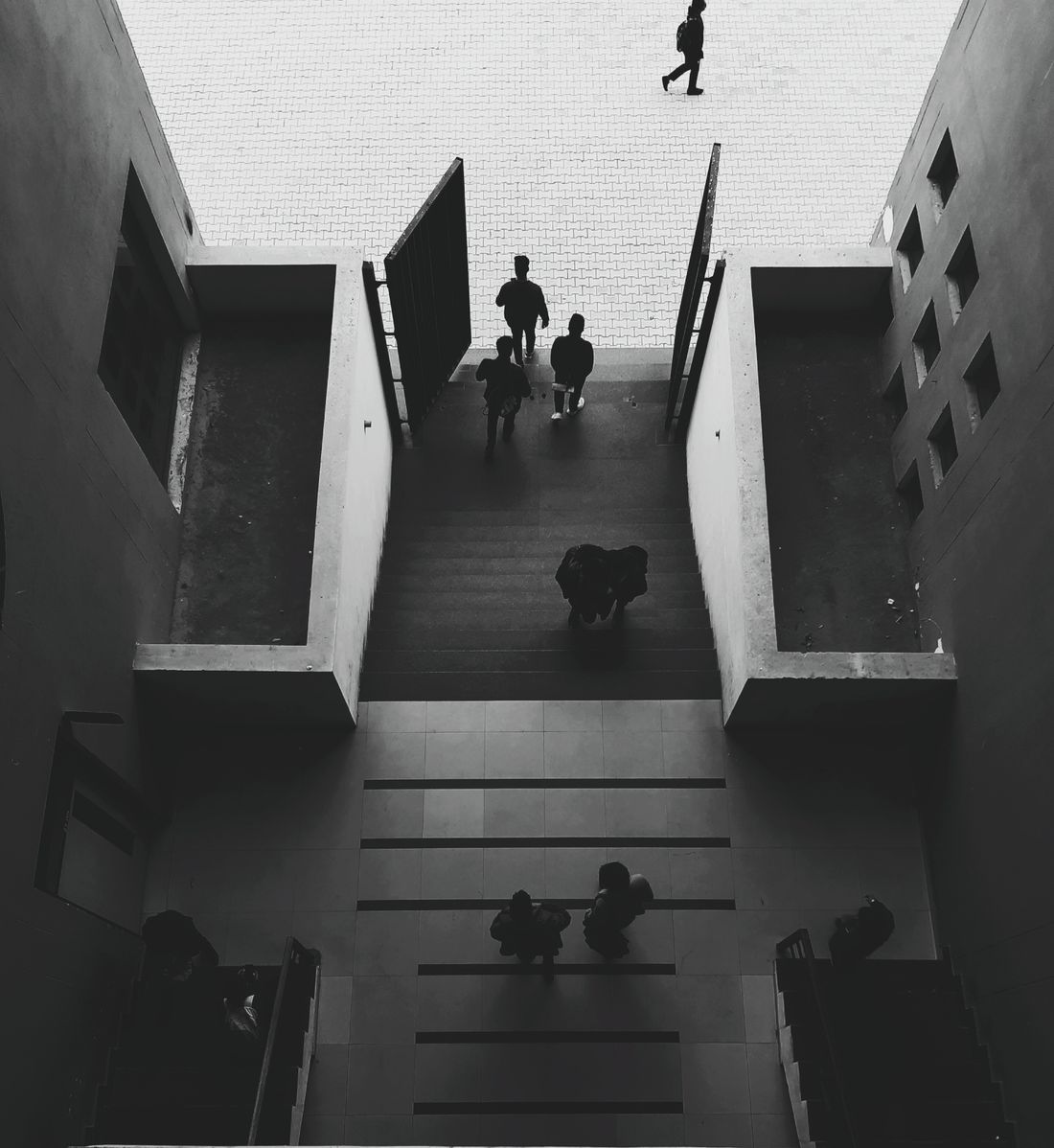 An overhead black-and-white view of visitors walking down an outdoor stairway toward a modern building entrance.