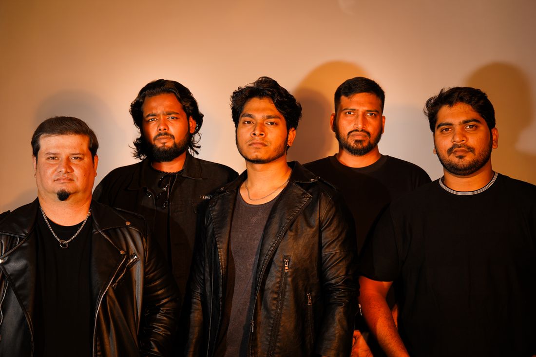 Five members of a band standing together for a group portrait, with one member lit and positioned as the visual center