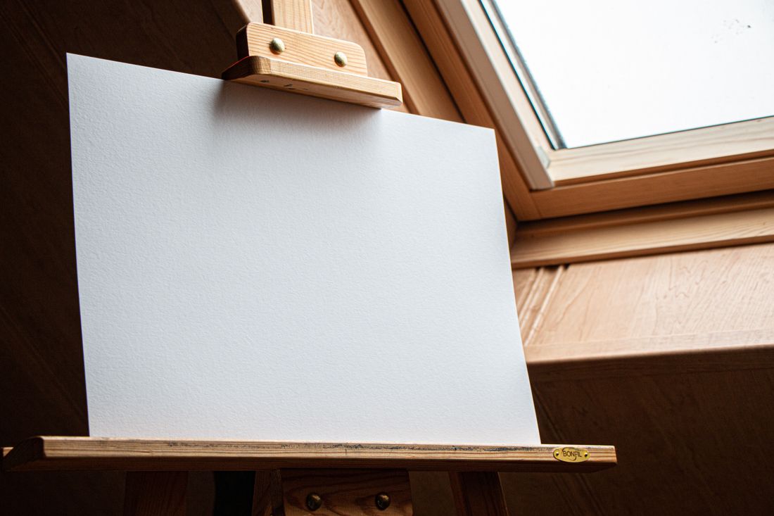 A blank canvas on a wooden easel lit by natural light through a skylight window