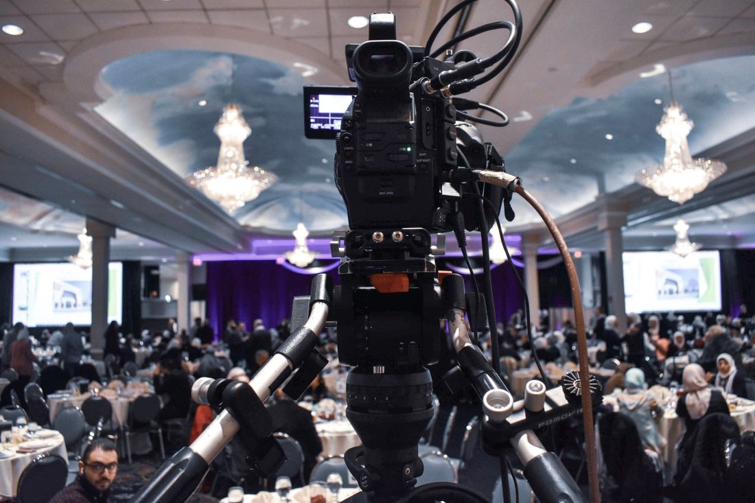 Professional video camera on a tripod recording a crowded event room