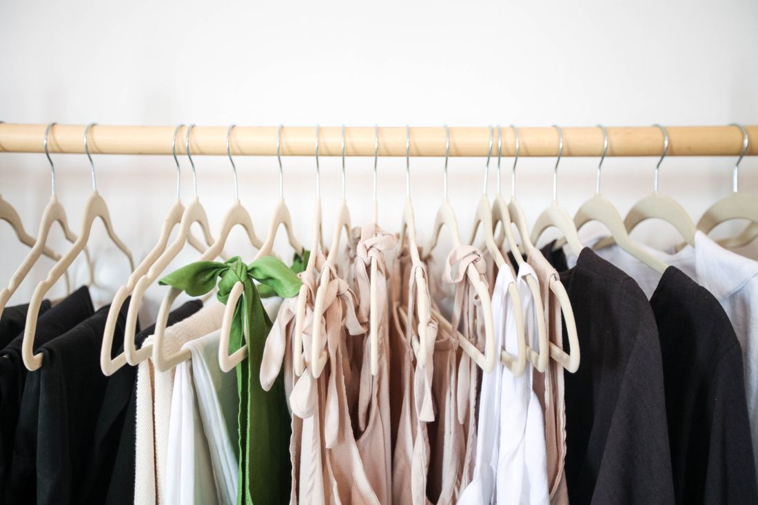A clothing rail of neutral-toned garments hanging against a plain pale wall