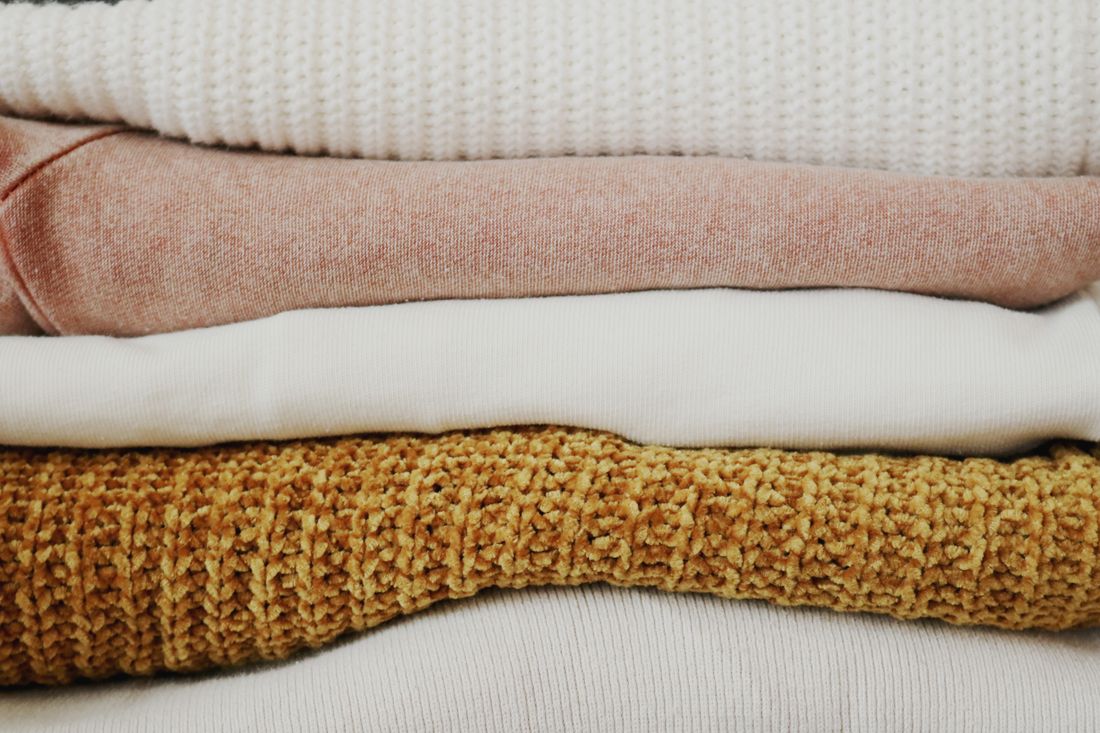 A stack of folded knitwear in soft neutral and ochre tones