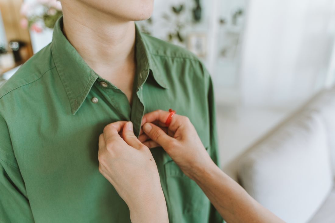 Hands fastening the buttons of a green cotton shirt, seen close and cropped below the face