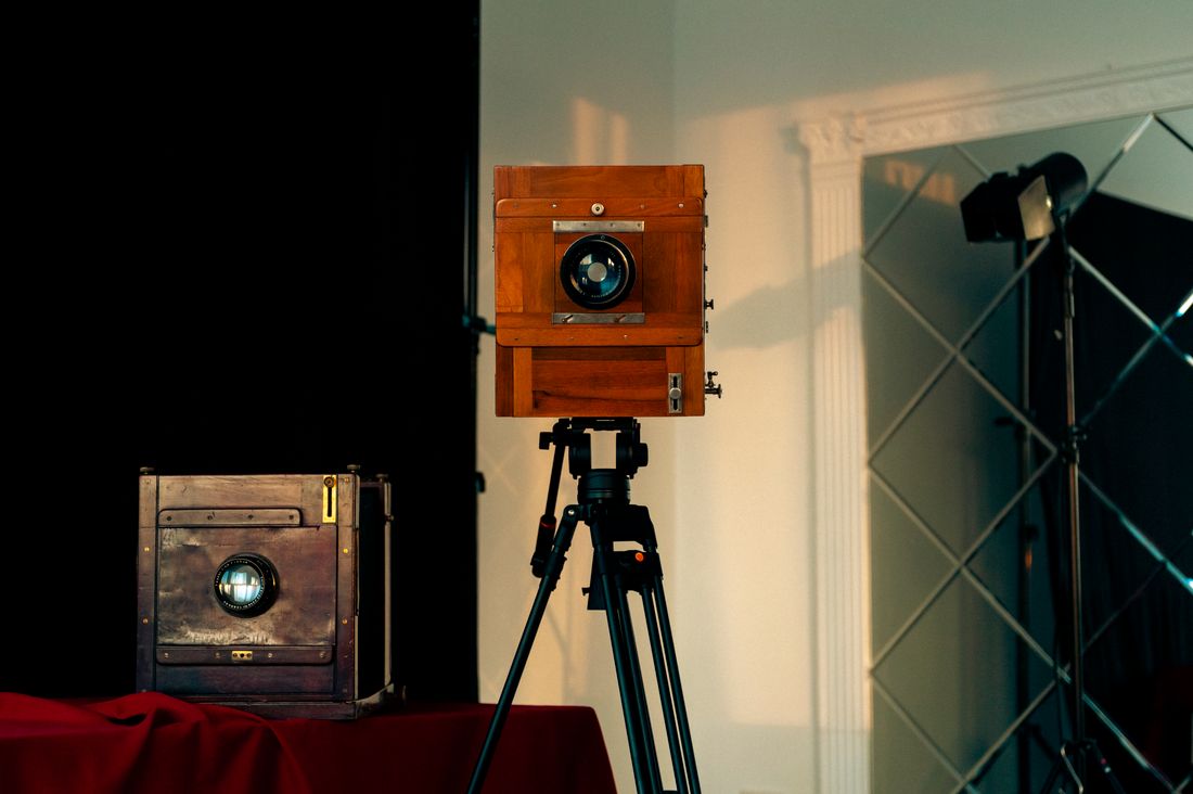 A large-format camera on a tripod set up indoors with a light stand behind it, mid-setup, no one in frame.