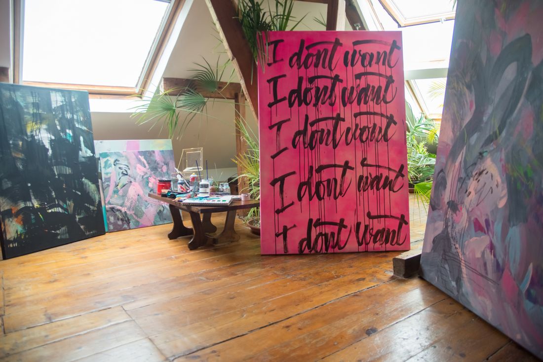 Several unframed canvases of different sizes leaning against the walls of a wood-floored attic room, with more work stacked behind them.