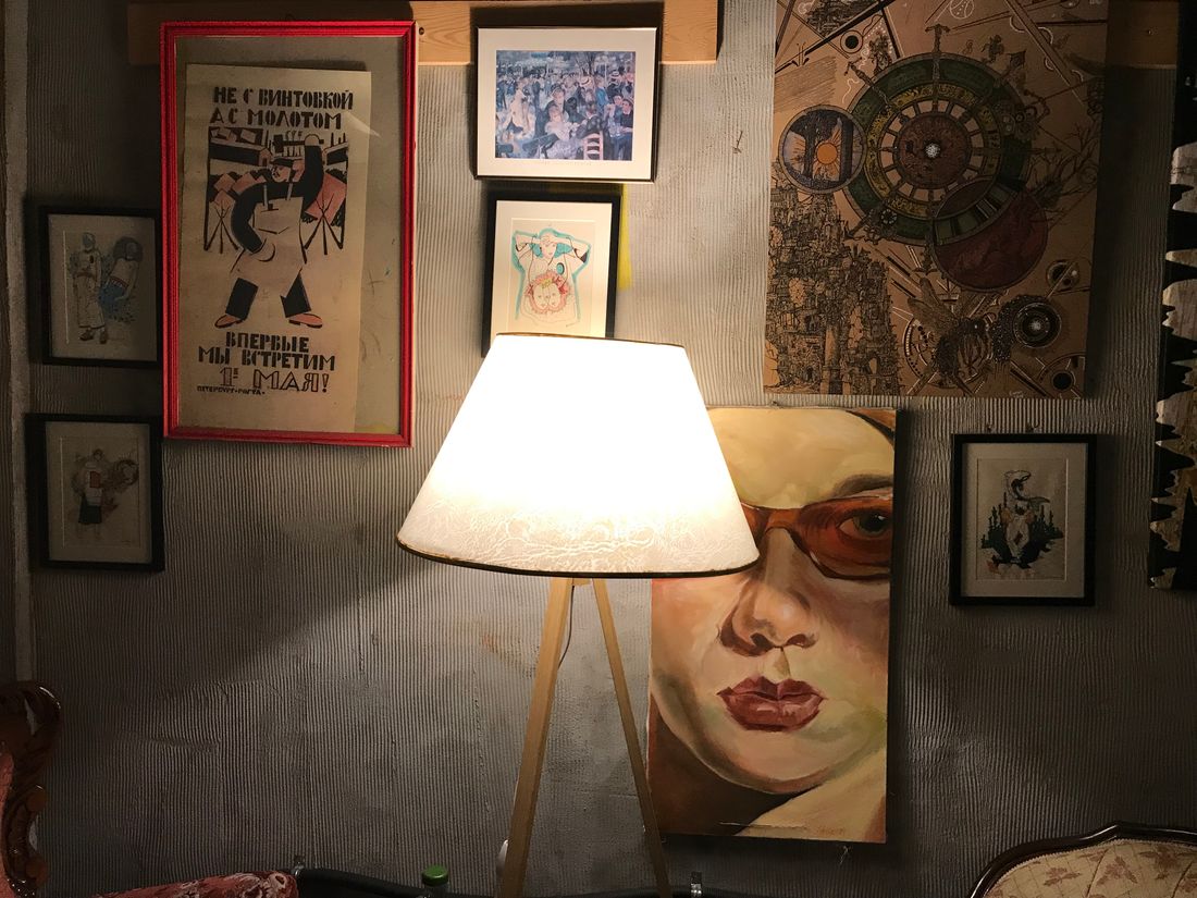 A wall of small framed pieces in many different sizes beside a large unframed canvas leaning behind a lamp.