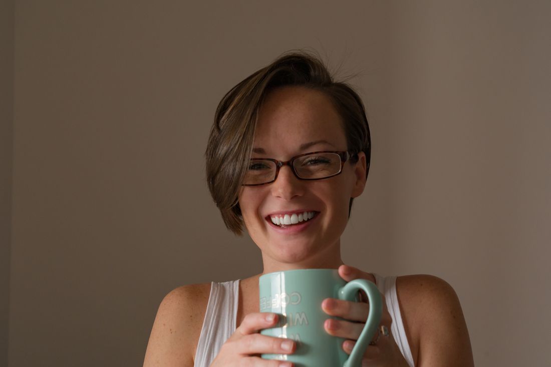 A woman laughing genuinely while holding a mug in soft natural indoor light