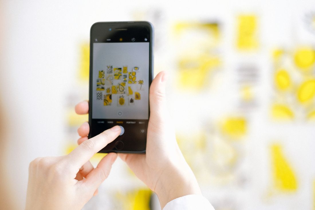 Close-up of hands holding a smartphone, photographing a colorful piece of artwork on a wall