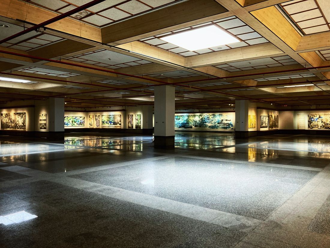 A large, empty gallery room with paintings on the walls under bright lighting before visitors arrive