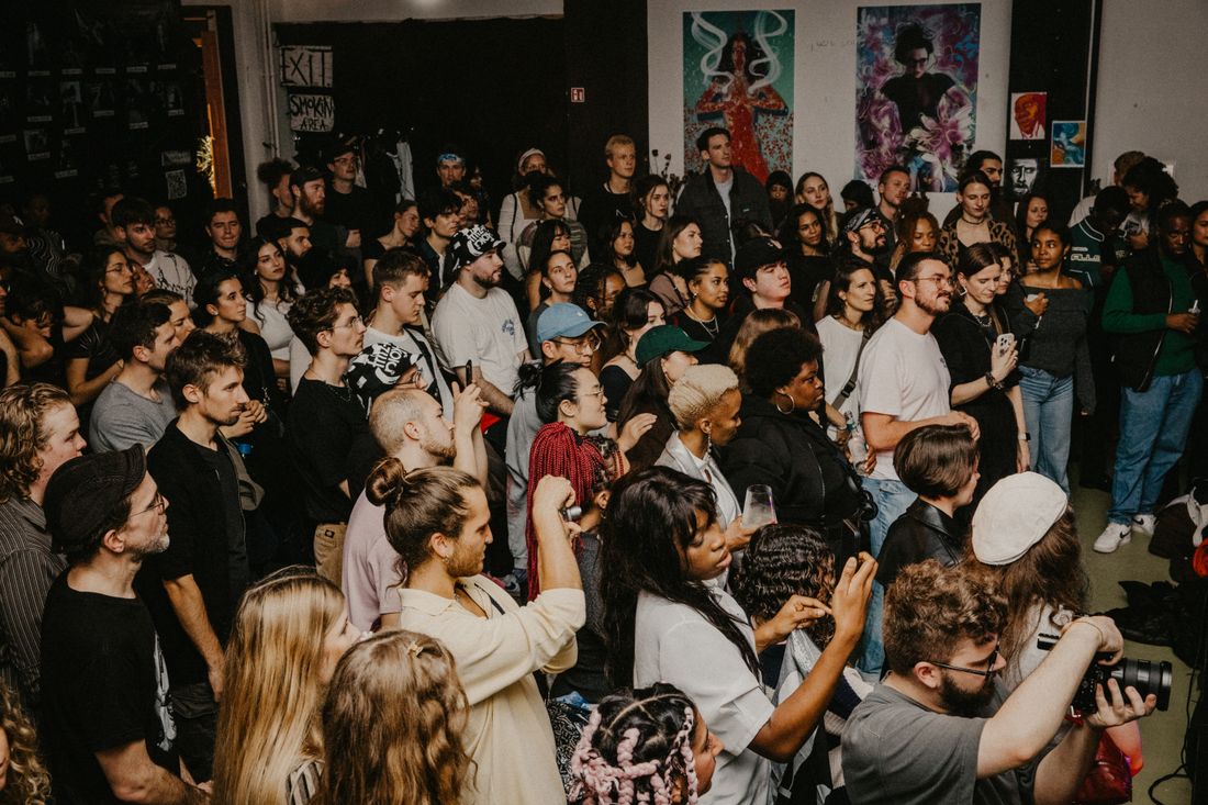 A dense crowd of people filling a room at an art event, some facing each other in conversation