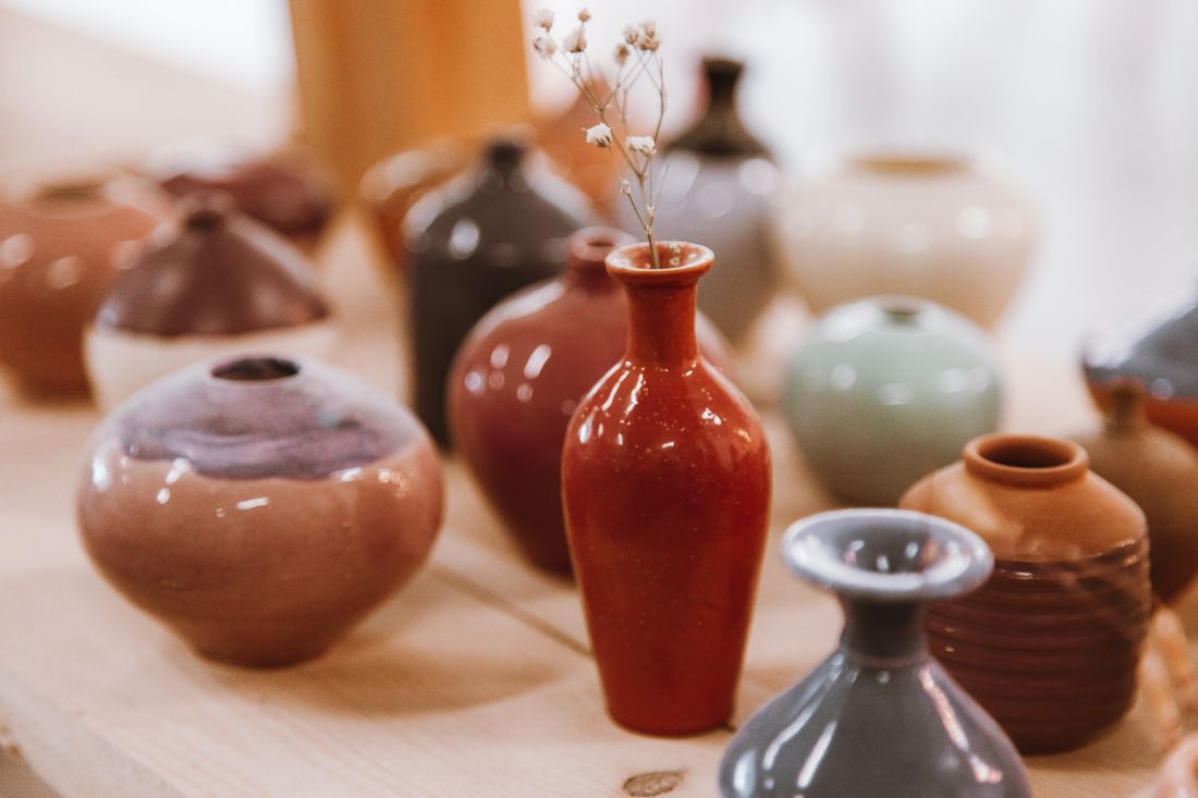 A close view of small handmade ceramic vases in varied glazes arranged on a wooden table