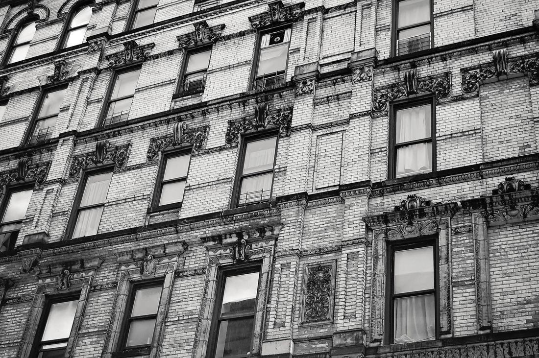 A black and white photo of an ornate pre-war NYC building facade with carved stone cornices and window surrounds