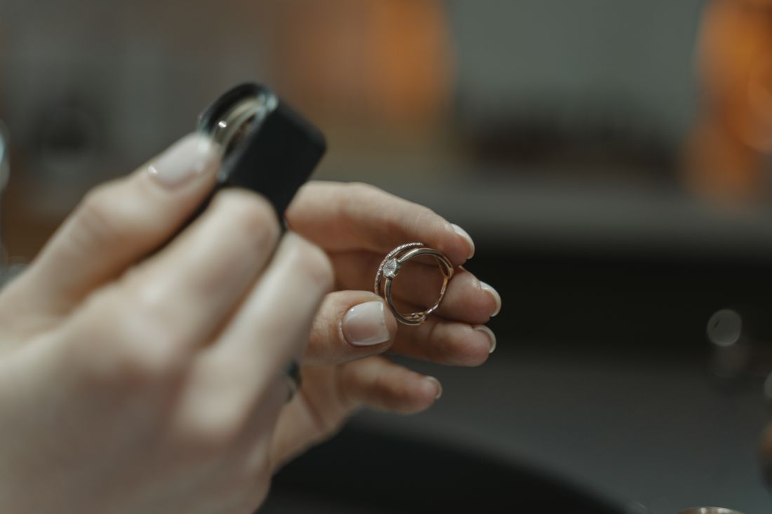 A close-up of two hands holding a small ring and a jeweler's loupe against a softly lit background