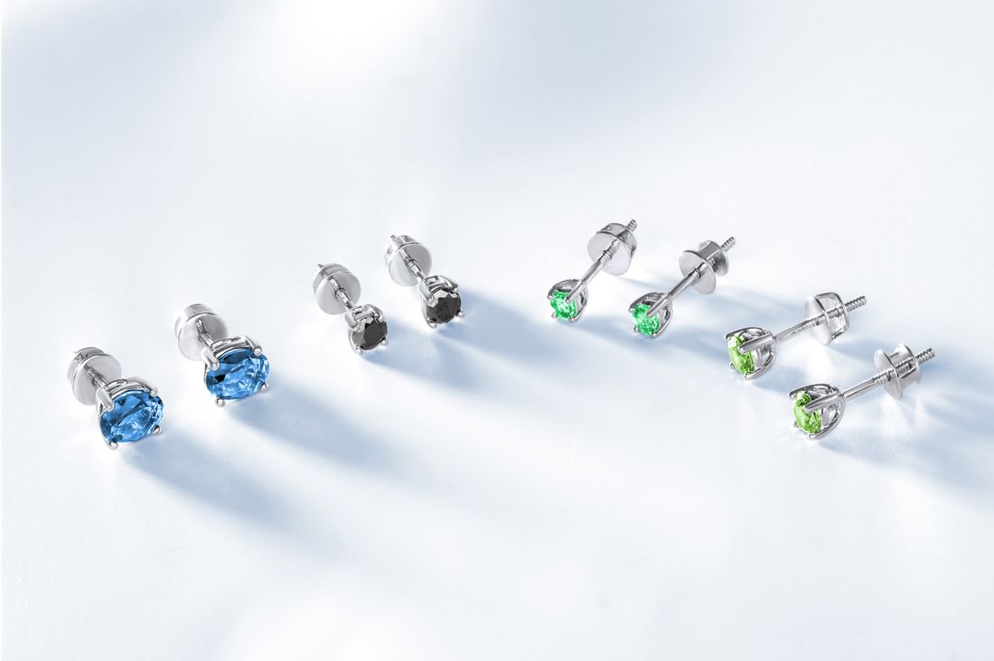 Several pairs of gemstone stud earrings arranged in a row on a plain white surface with soft shadows