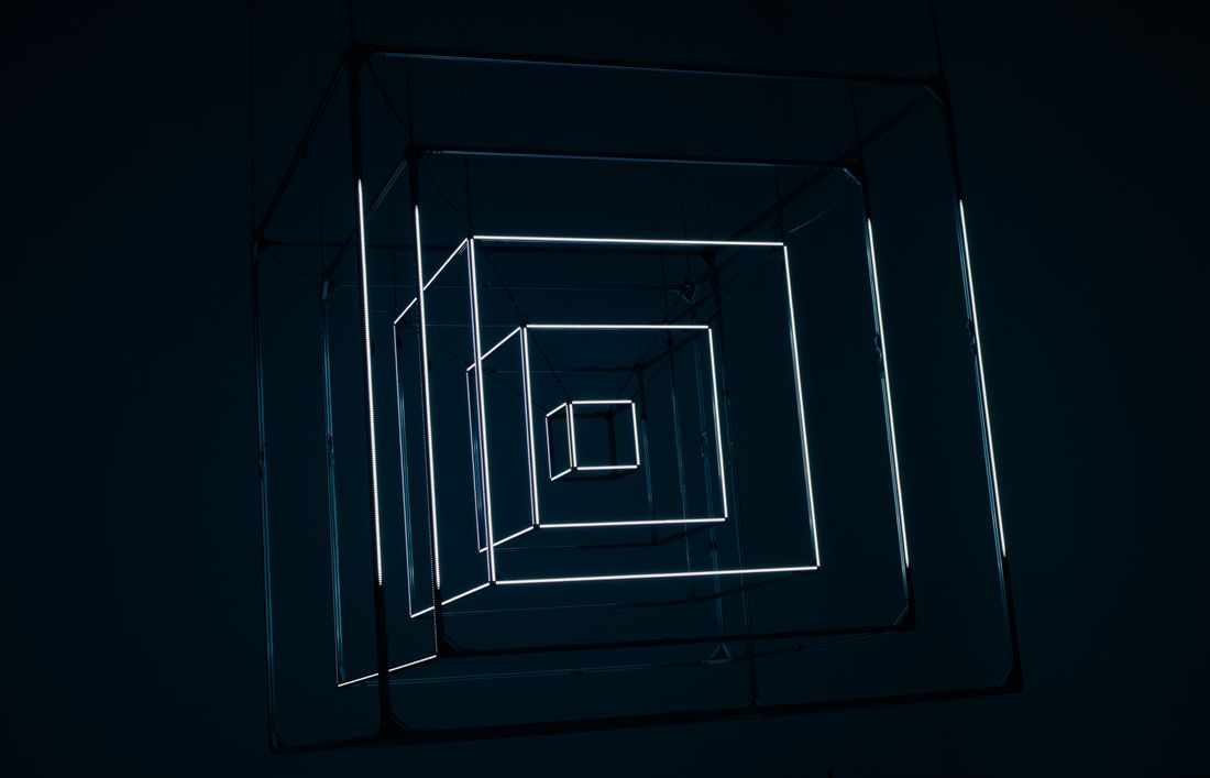 A glowing white geometric light installation forming nested squares in a dark room