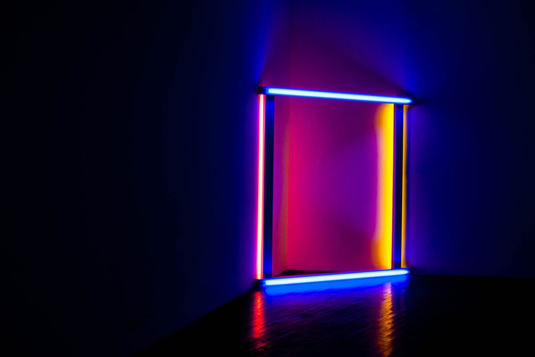 A colorful neon light installation in a dark room, its glow reflected on the floor and walls