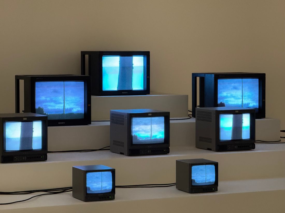 A group of boxy cathode-ray monitors arranged on pale plinths, each showing the same blue image, with black cables running between them.