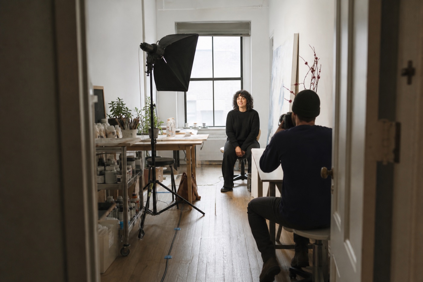 Photographer making a portrait with one compact soft light in a narrow contemporary NYC artist studio viewed through the doorway