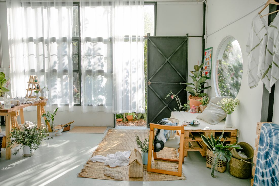 A bright studio room with a worktable, plants and materials in use beside tall windows